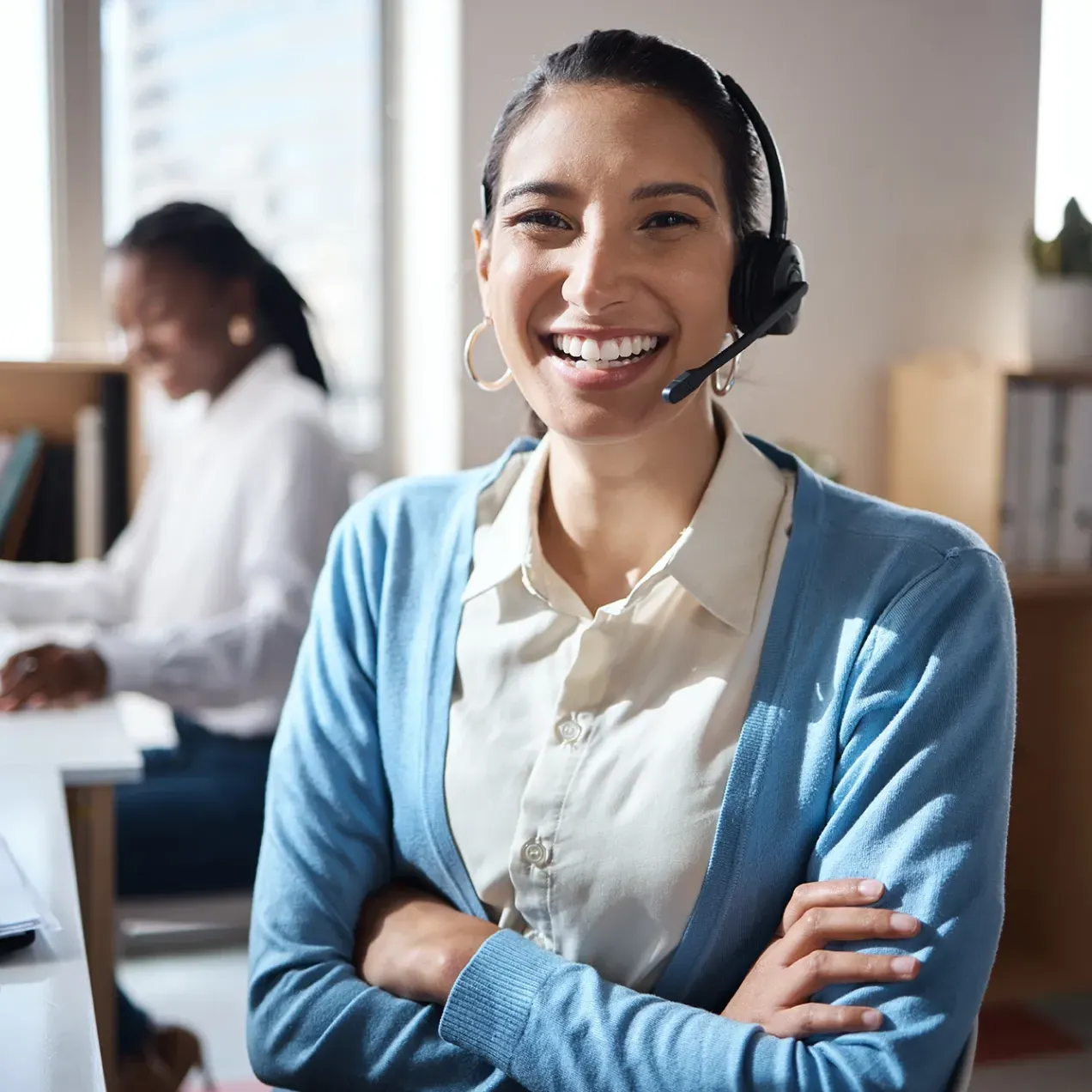 Friendly female receptionist wearing a headset, assisting a caller while working at a front desk in a medical or office setting.